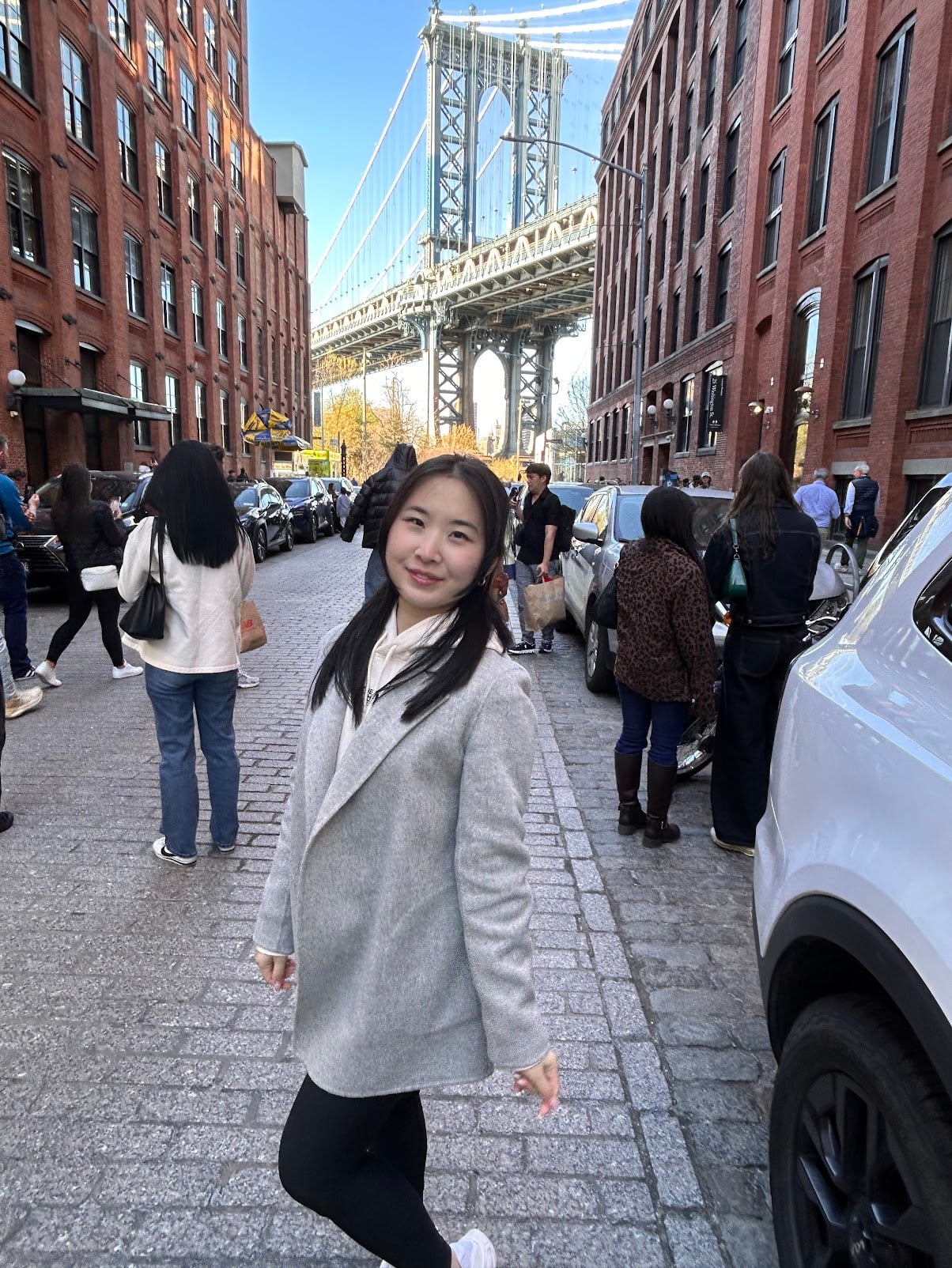 Kaitlyn smiling on a cobblestone street in Brooklyn, with the Manhattan Bridge behind her.