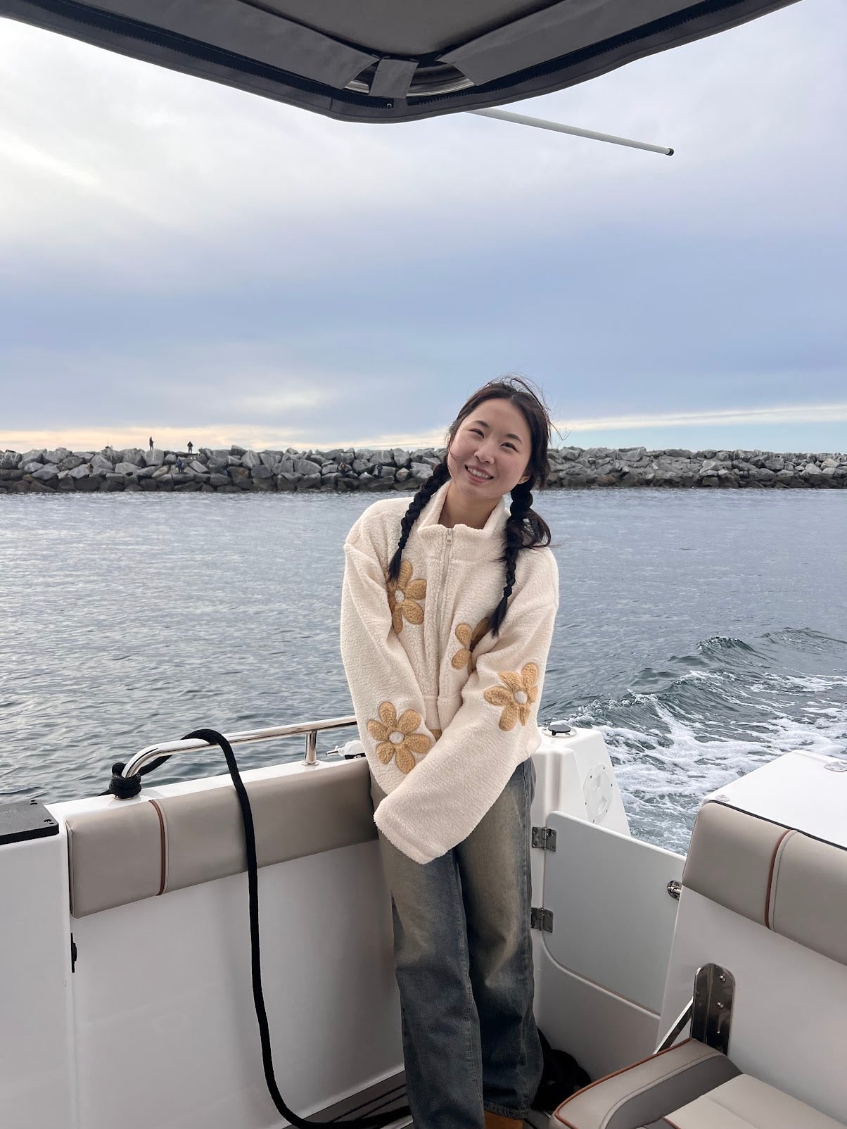 Kaitlyn smiling on the back deck of a boat, with the water and a rock jetty behind her.